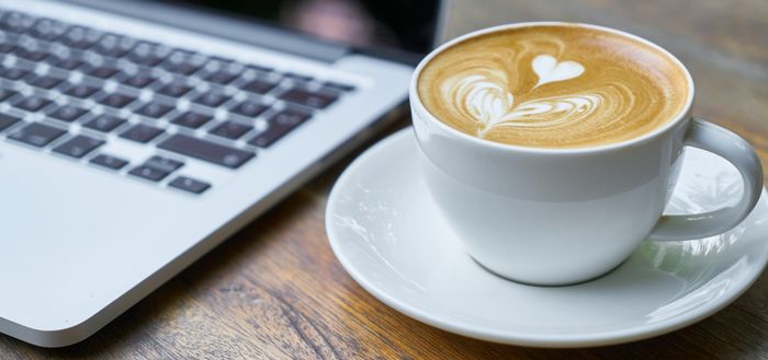 Coffee cup, drizzled with creamy milk and heart shape next to a laptop computer'
